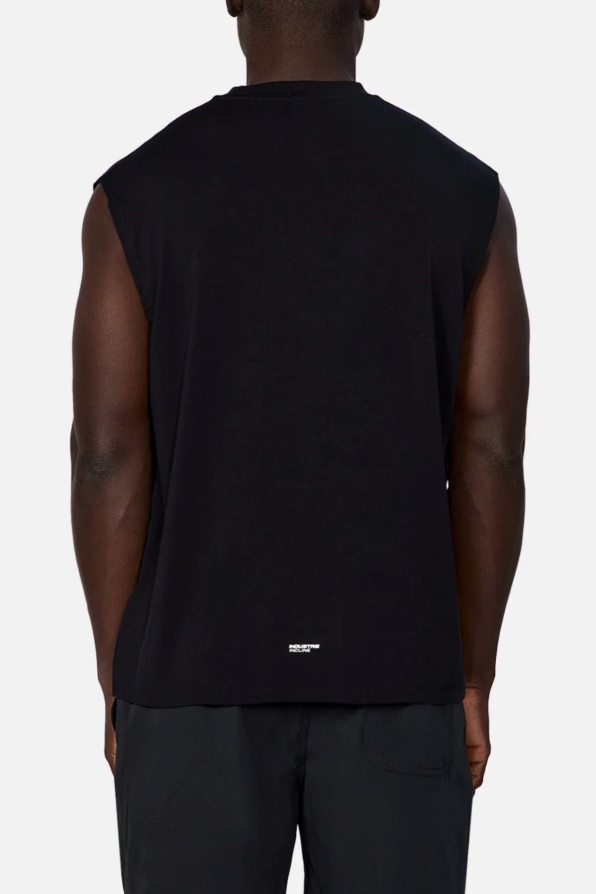 A person is seen from the back wearing the Industrie The Freeman Sleeveless Tee in black and matching black pants. The plain, light background highlights a small white label near the hem of the quick-dry shirt.