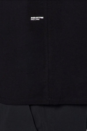Close-up of the Industrie The Freeman Sleeveless Tee in black, featuring a small white "INDUSTRIE INCLINE" logo on the chest, center seam detail, and quick-dry technology—styled with dark pants, ideal for workouts.