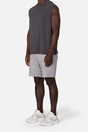 A man wears the Industrie The Freeman Sleeveless Tee in dark gray, light gray shorts, and white sneakers, standing against a plain white background with his face out of frame.
