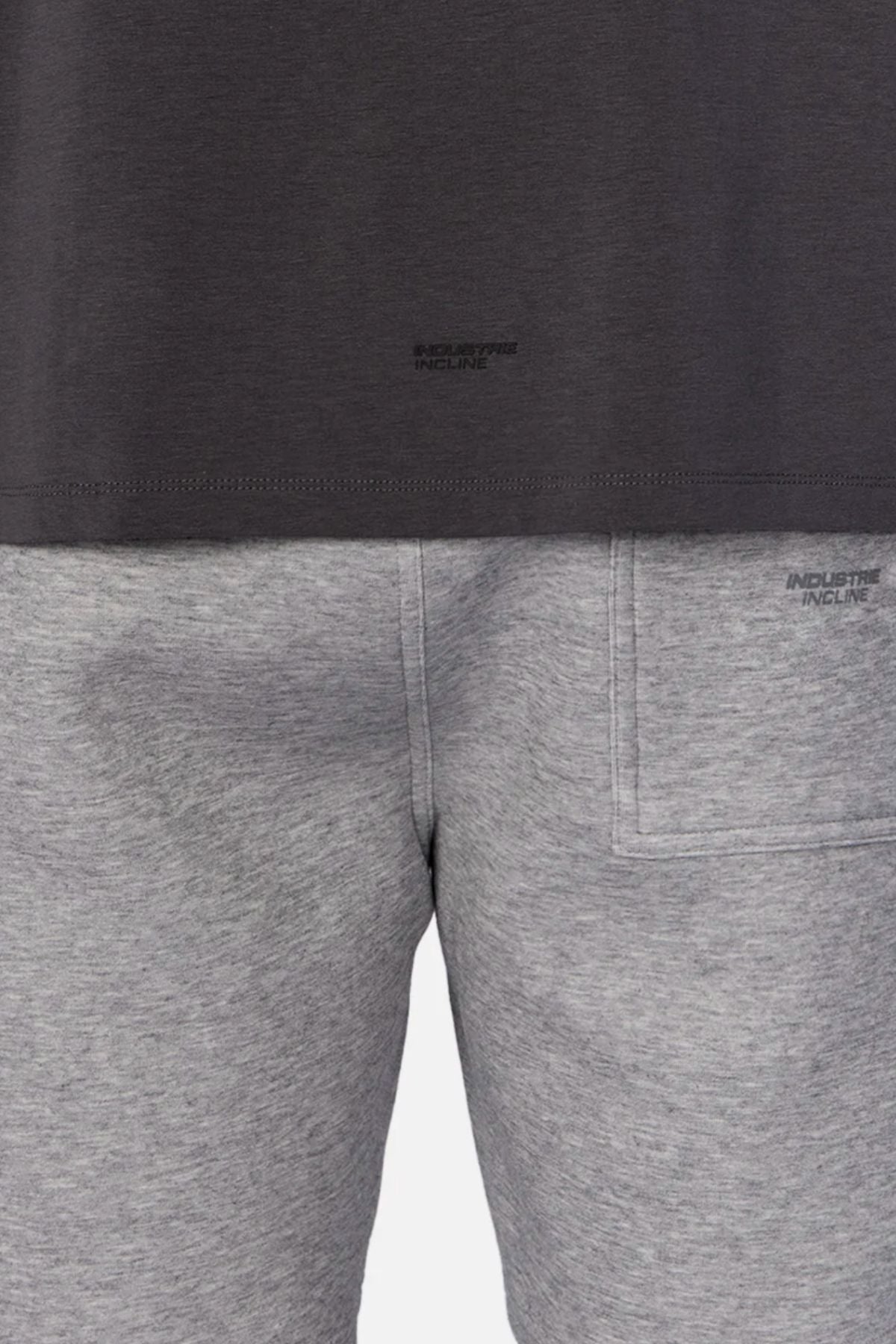 A person wears the Industrie The Freeman Sleeveless Tee in dark gray and light gray sweatpants with a back pocket, quick-dry fabric, and a visible wet stain on the left side, shown from waist to mid-thigh.