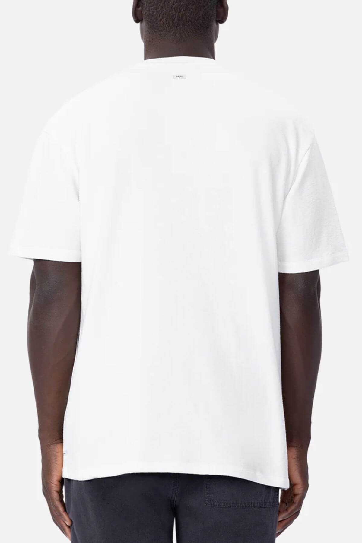 The person is wearing an oversized Industrie The Henderson Boucle Tee in plain white, seen from the back with hands relaxed. The soft grayish-white backdrop highlights the comfortable and relaxed style of this 100% cotton tee.