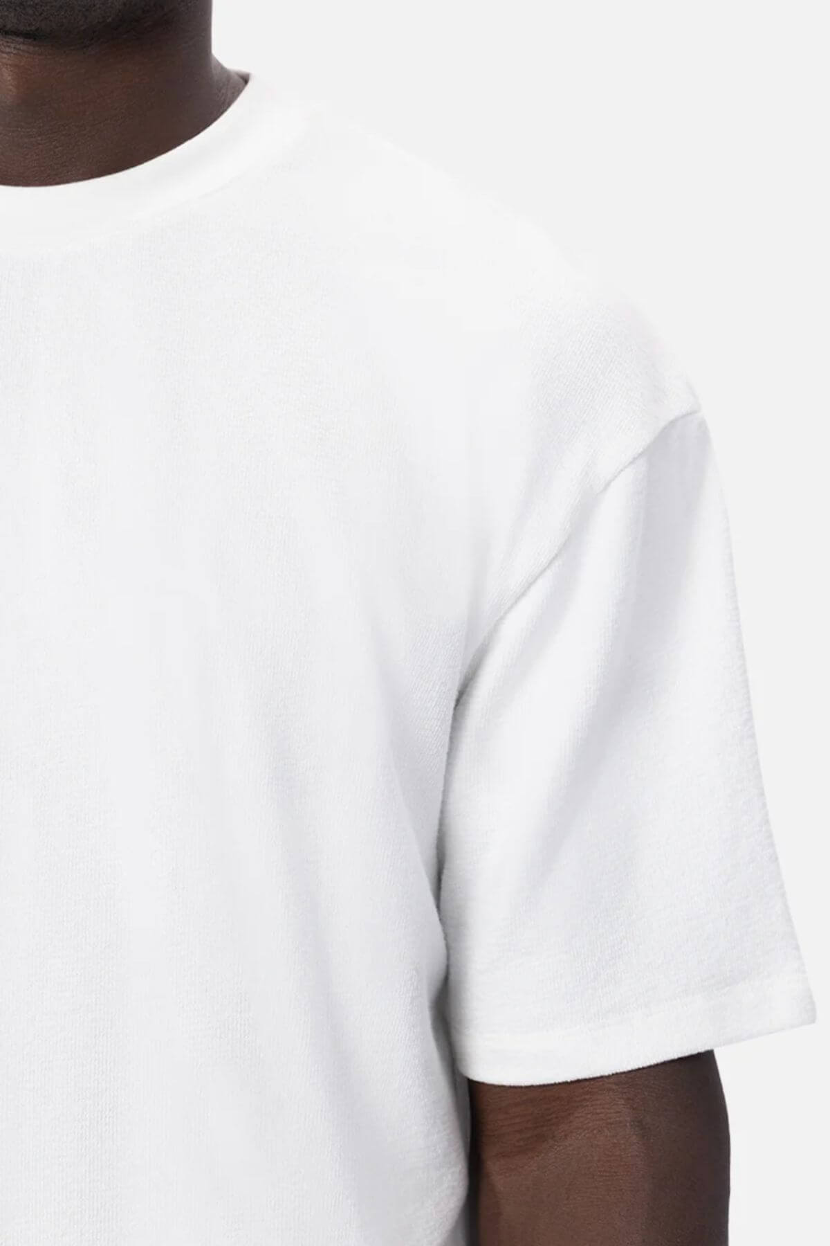 Close-up of a person in an oversized fit Industrie The Henderson Boucle Tee in plain white, highlighting the upper right section of the 100% cotton tee and part of their arm against a plain background.