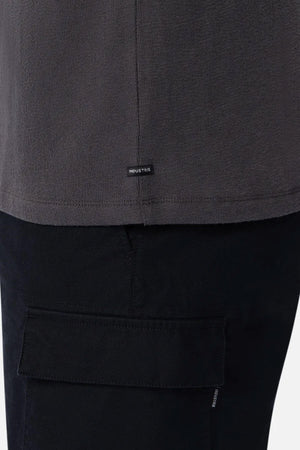 Close-up of a person wearing the Industrie The Henderson Boucle Tee in dark gray, oversized fit, paired with black flap-pocket pants. A small black "INDUSTRIE" tag is sewn near the shirt’s bottom hem.