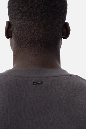 A person with short, curly hair is seen from behind, wearing the Industrie The Henderson Boucle Tee—an oversized dark gray sweater with a small black "INDUSTRIE" label on the back collar. The background is plain white.