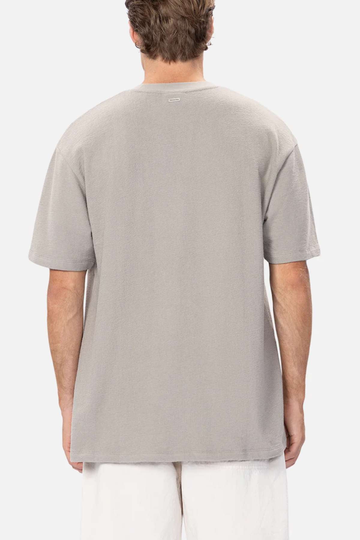 An individual with short hair is wearing an oversized, light gray Industrie The Henderson Boucle Tee (100% cotton) paired with white pants. Facing away from the camera, they showcase the relaxed back view of the outfit against a plain white background.