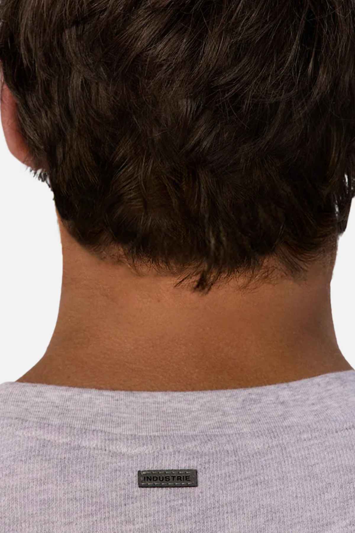 The image depicts the back of a person's head with short dark hair. They are dressed in an oversized, light gray shirt made entirely from cotton, featuring a small black label that reads "INDUSTRIE" on the back of the collar. This garment is similar to the Industrie The Henderson Boucle Tee style.