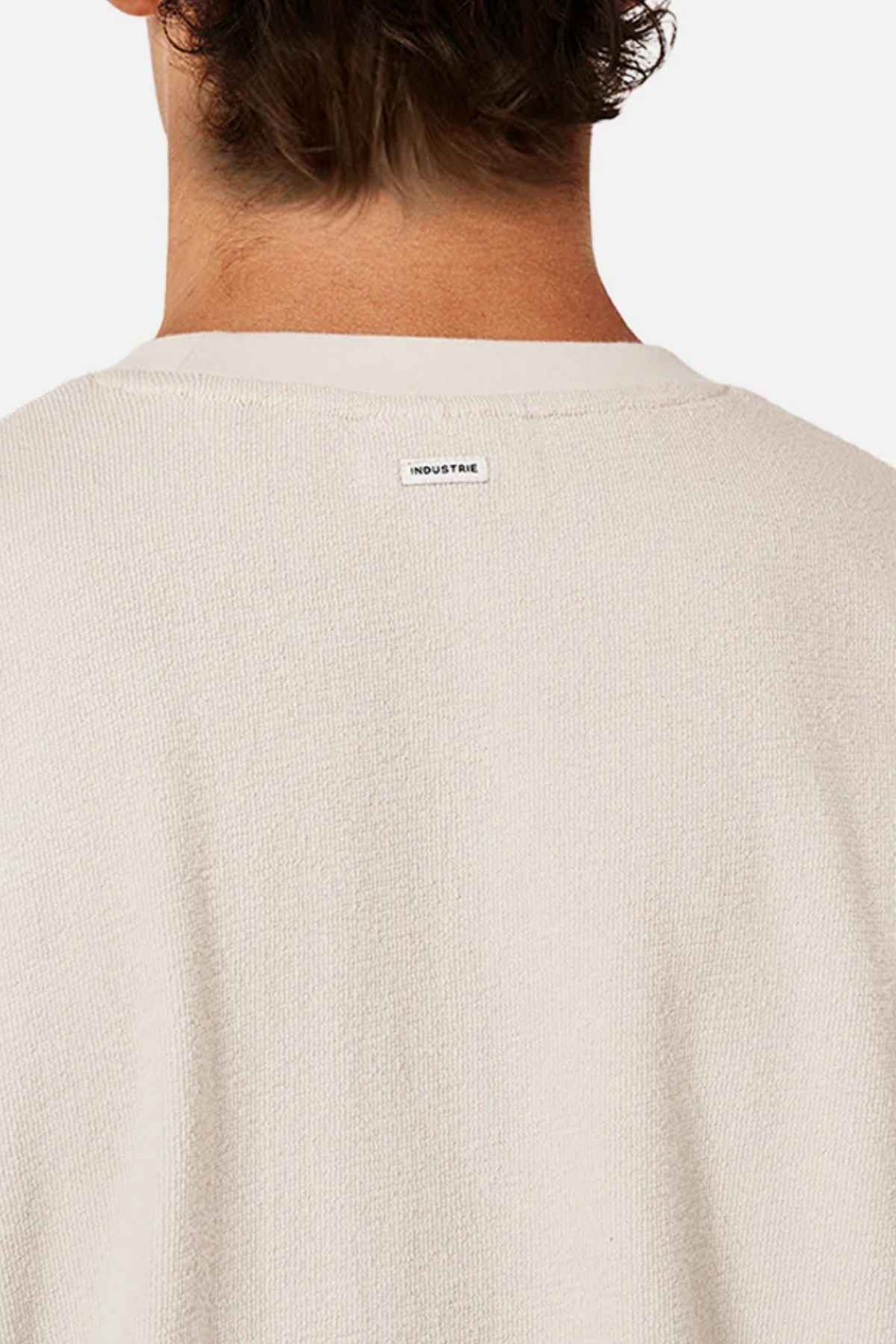 A person with short, curly hair is shown from the back, wearing an oversized cream-colored sweater made of 100% cotton. A small label reading "INDUSTRIE" is visible on the upper back. The plain white background accentuates the cozy texture of the Industrie The Henderson Boucle Tee.