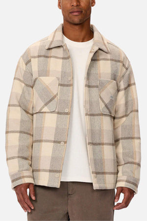 Sporting the Industrie The Hillside Jacket, a beige and gray check pattern button-up featuring two chest pockets over a crisp white shirt, teamed with brown pants on a plain white backdrop, this ensemble perfectly melds style and comfort.