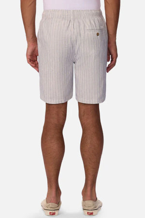 A man faces away, wearing Industrie The LA Brava Short—light gray and white vertical striped linen-blend men's casual shorts with a buttoned back pocket, paired with a tucked-in white shirt and beige slip-ons against a plain white background.