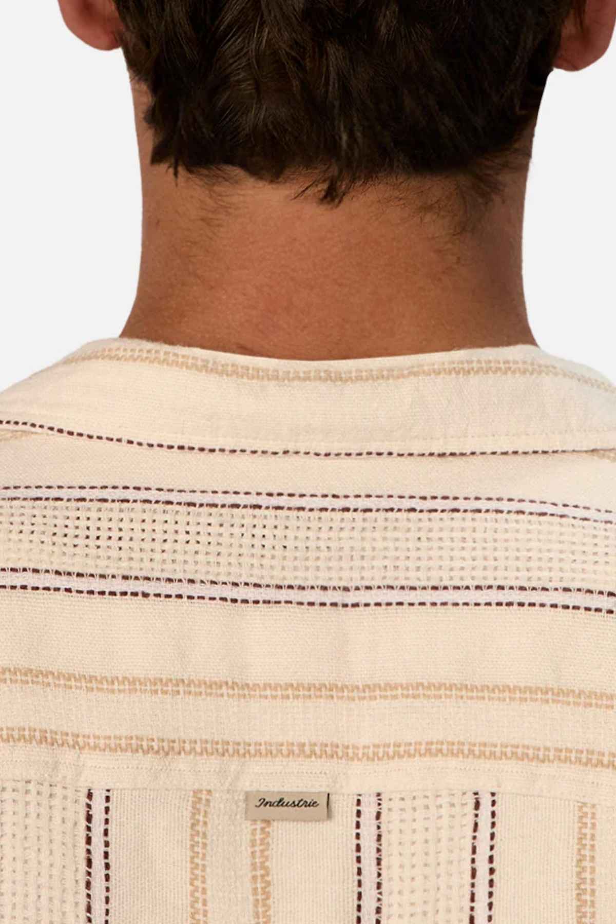 Back of a person wearing the Industrie The Lakeville Short Sleeve Shirt, crafted from a linen viscose blend in cream with horizontal brown stripes. A small label is visible, showcasing the brand name "IndusDiva.