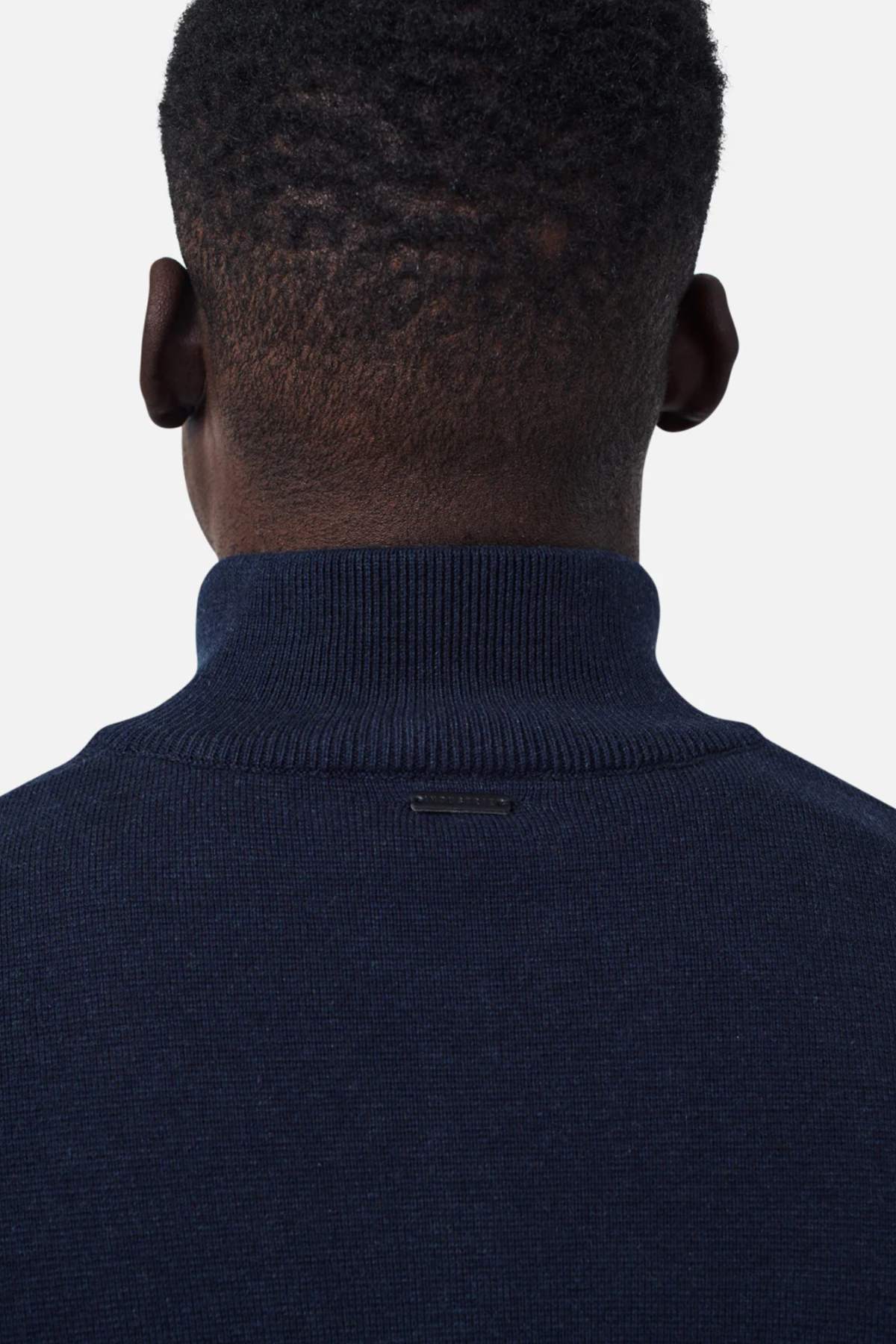 The image shows the back of a person's head and upper shoulders. The person is wearing an Industrie The Lakewood Zip Neck jumper in dark navy blue with a high collar and has short, closely-cropped hair. The background is plain and white.