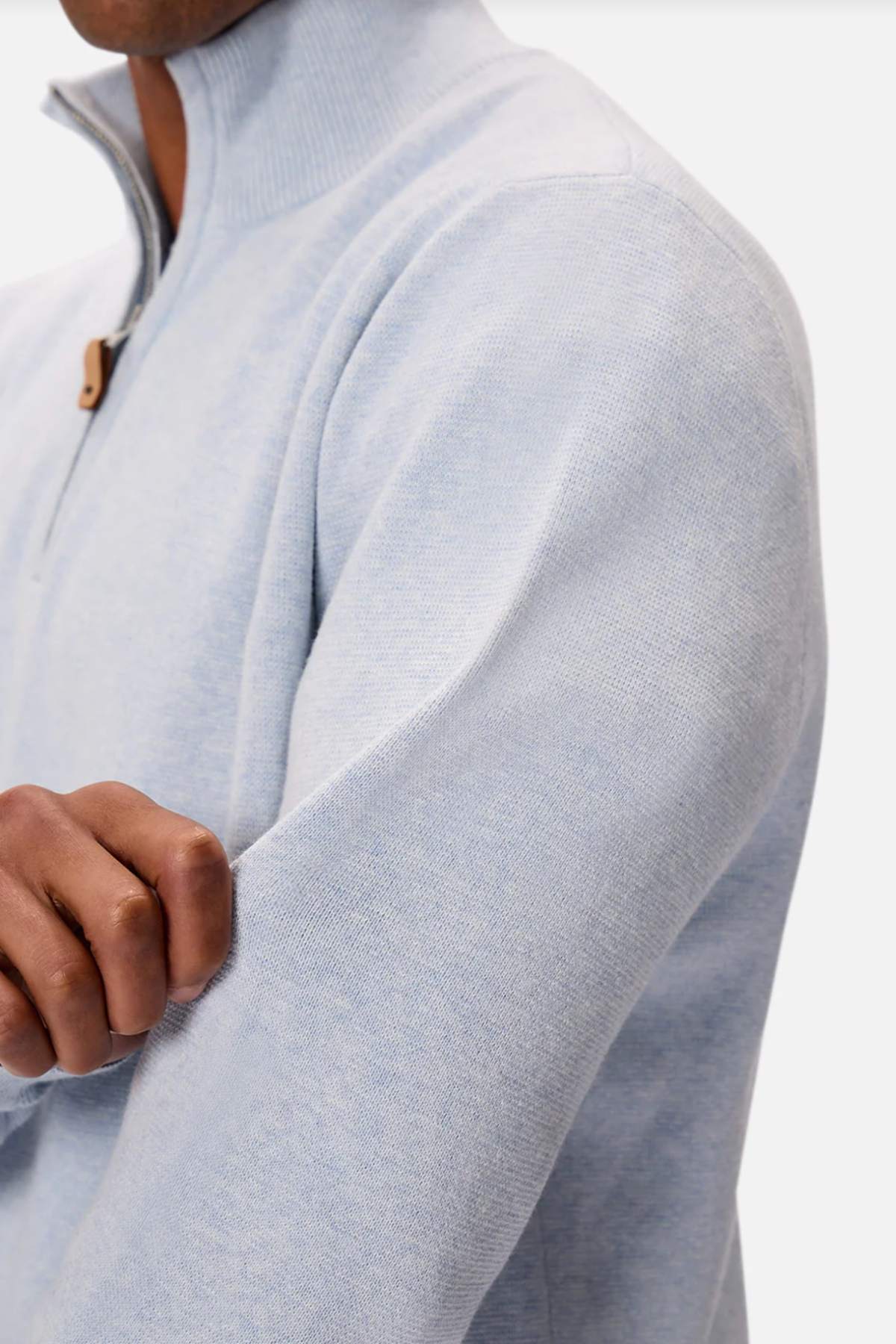 A person dons the Industrie The Lakewood Zip Neck, a light gray cotton jumper with a zip neck and high collar. While pulling on the sleeve, they highlight its subtle texture, regular fit, and small leather tab on the zipper.