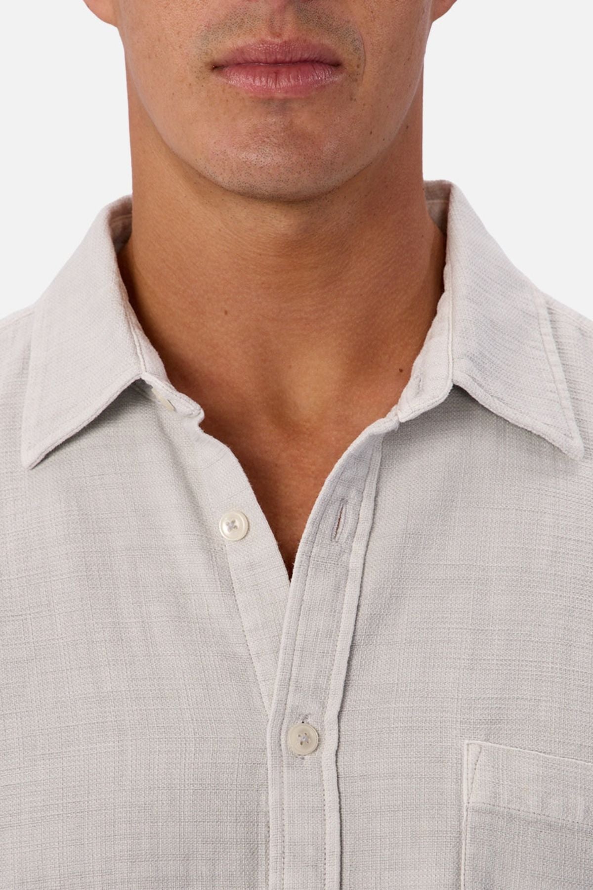 Close-up of a person wearing the Industrie Lisbon Long Sleeve Shirt, a light-colored, textured 100% cotton button-up with an open collar. Only the lower half of the face, neck, and upper chest are visible.
