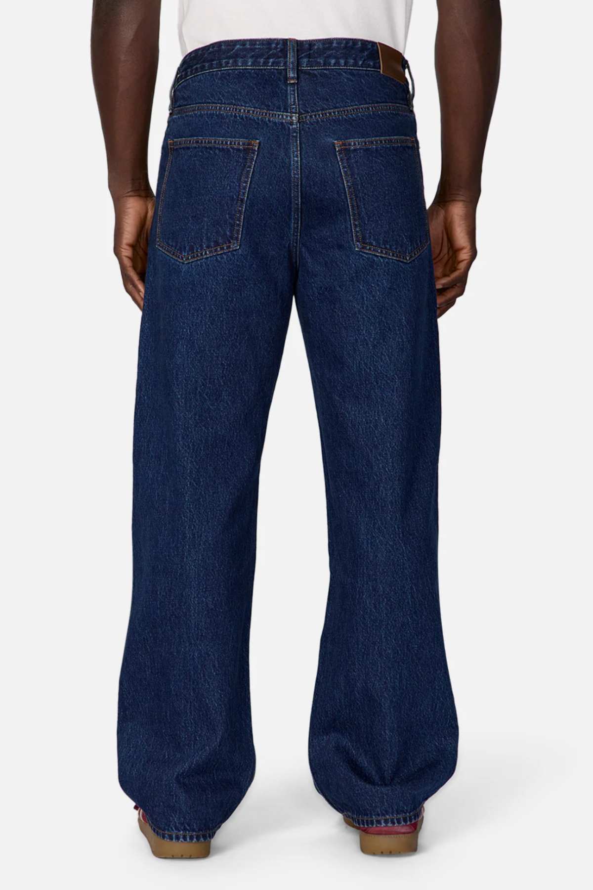 A person wearing the high-waisted, wide-leg Industrie The Lone Star Jean in dark blue. These loose-fitting jeans feature two large back pockets and visible orange stitching. The person is standing with their back to the camera against a plain background.