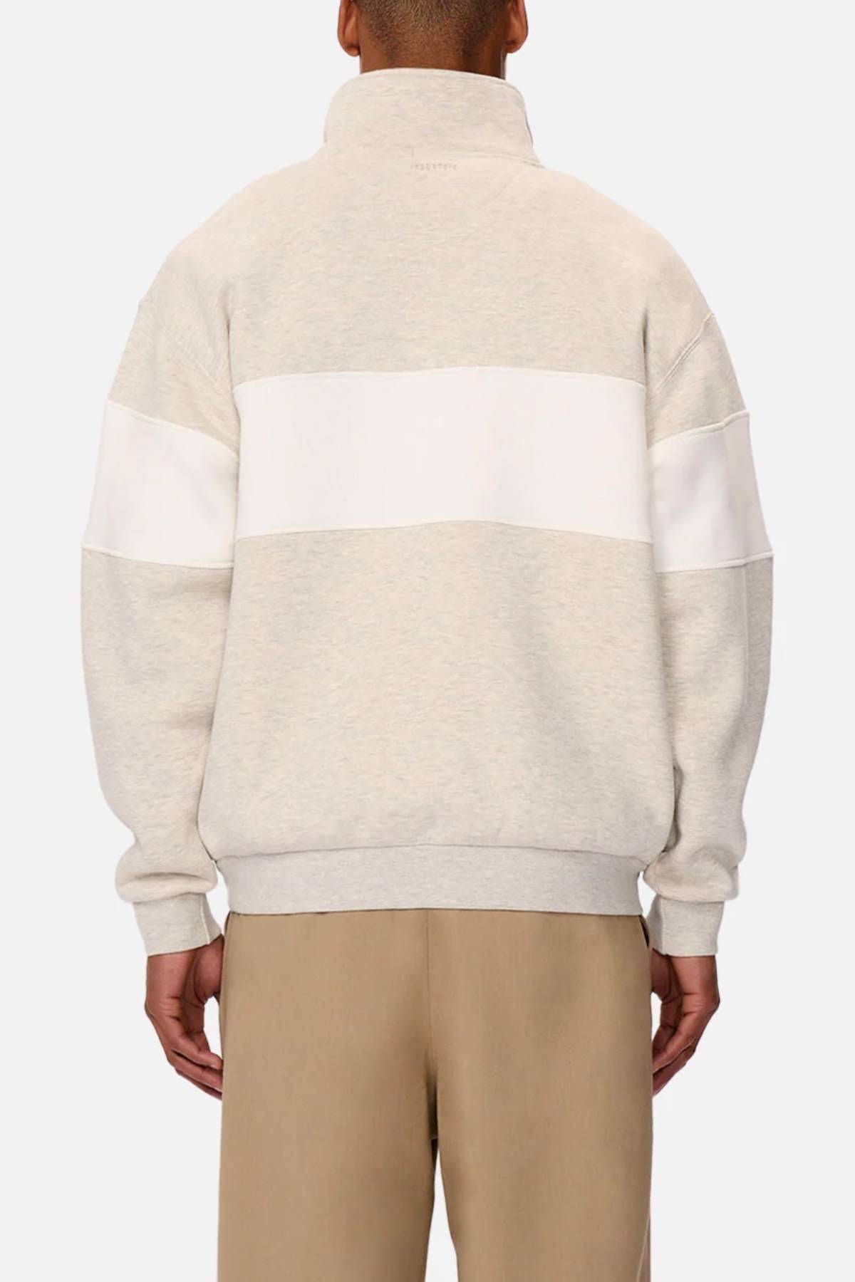 A person is seen from behind wearing a light beige and white Industrie The Luton Track Top, featuring a high collar and quarter zip neck, with long sleeves. They are paired with khaki pants against a plain white background.