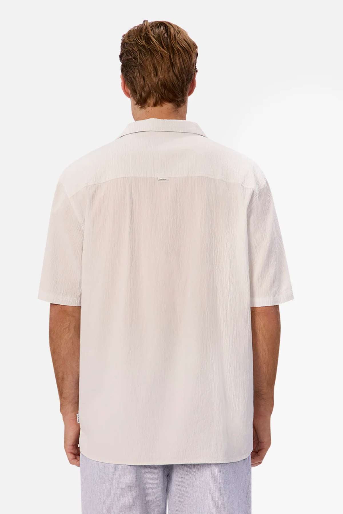 Rear view of a person wearing an oversized fit, light beige Industrie The Magna Short Sleeve Shirt paired with light gray pants. Made from 100% cotton, the fabric's texture stands out against a plain white background.
