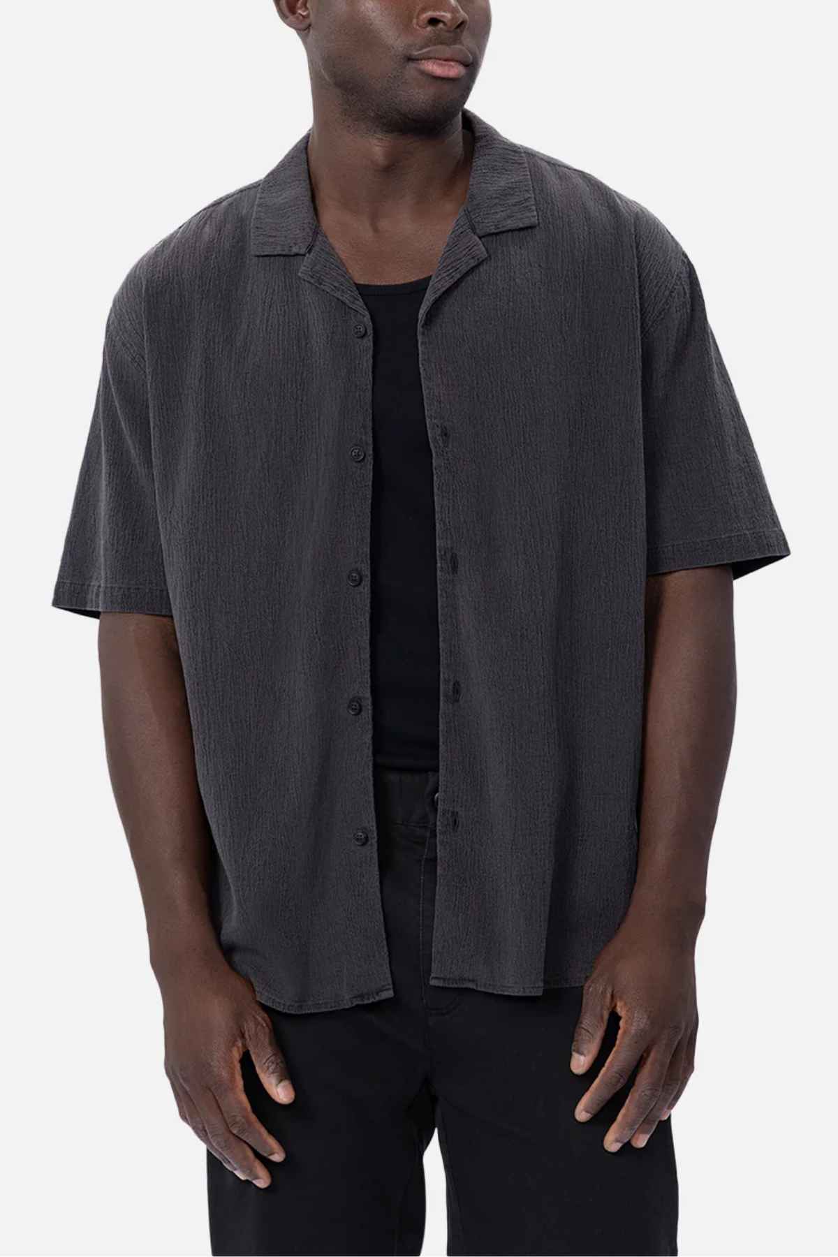 A person wearing the Industrie The Magna Short Sleeve Shirt in charcoal gray, styled oversized over a black T-shirt, stands against a plain white background.