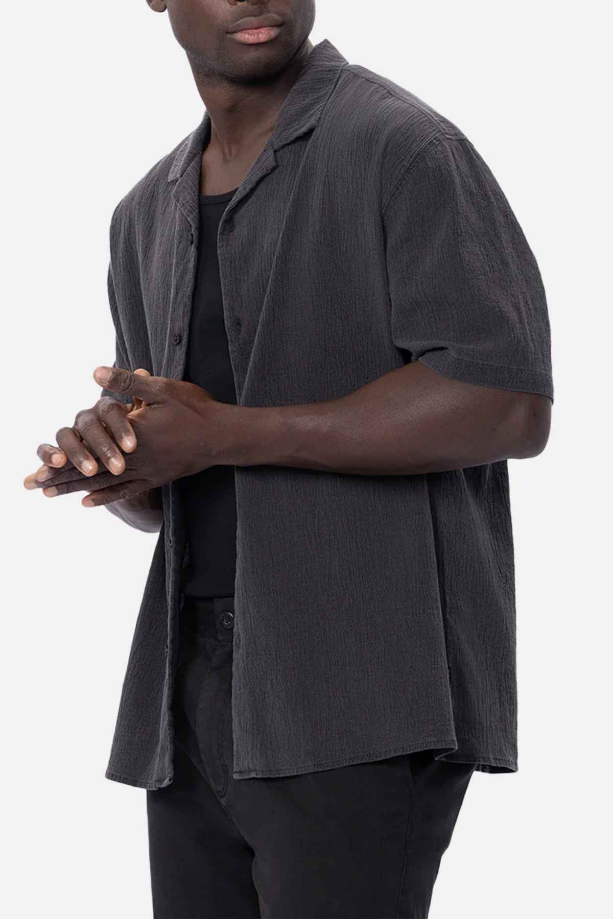 A person wearing the Industrie The Magna Short Sleeve Shirt, characterized by its oversized fit and dark, textured short sleeves made from 100% cotton, stands against a plain background. They clasp their hands together while looking slightly to one side.