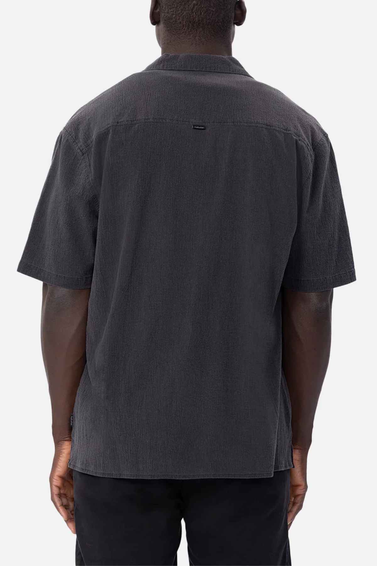 Rear view of a person wearing the oversized Industrie The Magna Short Sleeve Shirt in dark gray, made from 100% cotton, paired with black pants, standing against a plain white background.