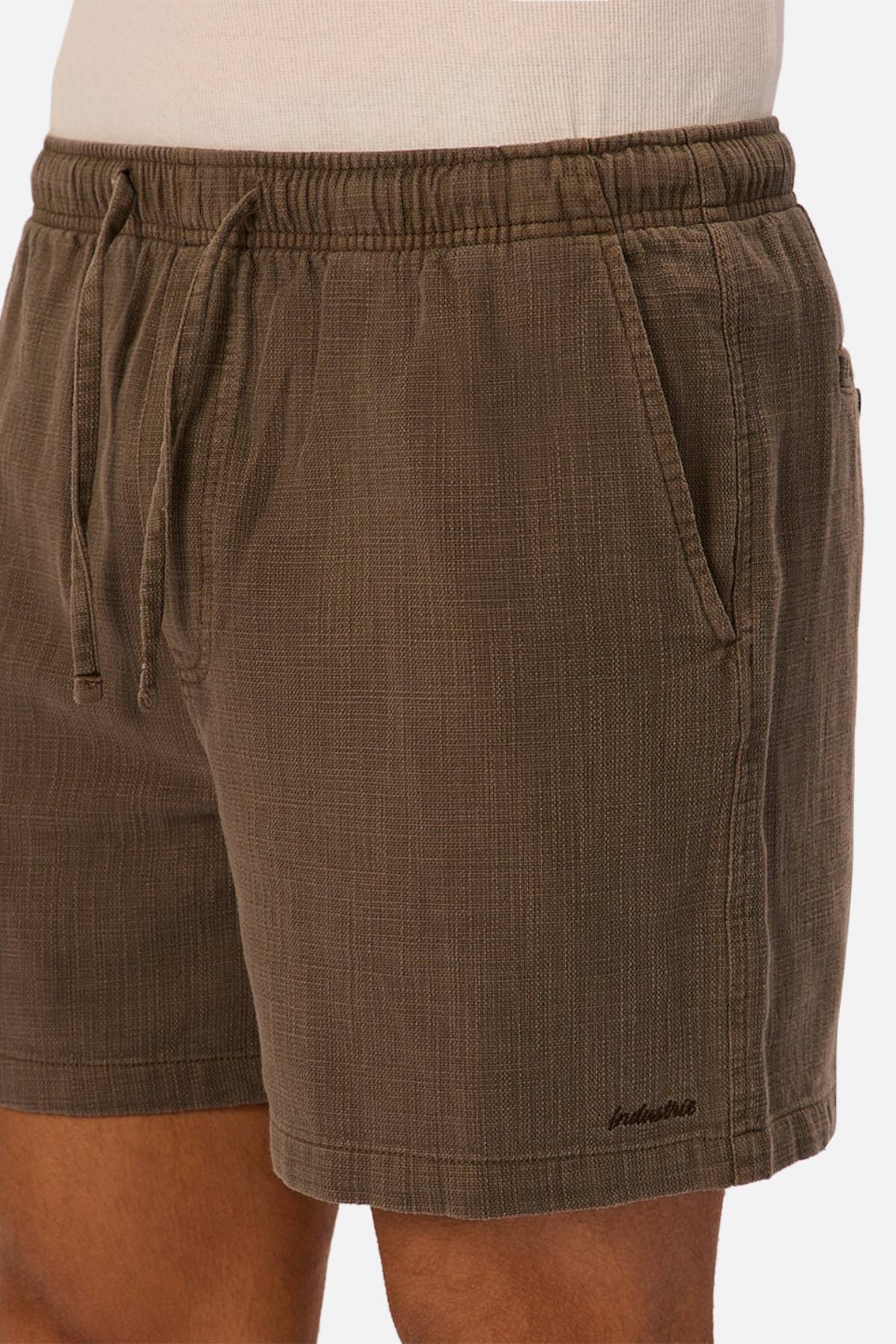 A person wearing Industrie The Mallorca Short, made from lightweight textured fabric with an elasticated waist, side pockets, relaxed fit, and subtle embroidery near the hem, paired with a white shirt.