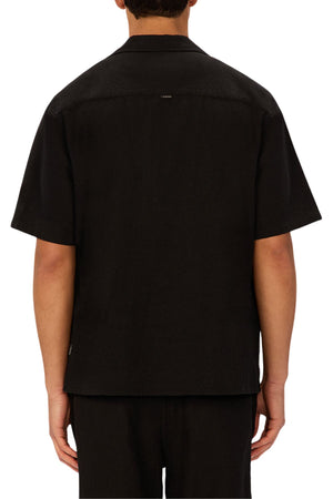 A person is seen from behind wearing the Industrie The Marbella Short Sleeve Shirt in black, which has a relaxed fit, short sleeves, and a straight hem, paired with matching black pants against a plain, neutral background.