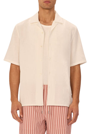 A man models the Industrie The Marbella Short Sleeve Shirt in a relaxed fit, cream color, layered over a white tee and light red, striped shorts—standing forward with hands at his sides, highlighting a casual, everyday look.