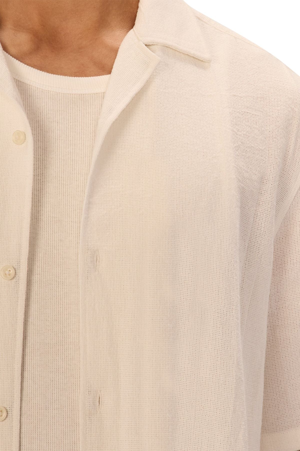 A close-up of a person wearing the Industrie The Marbella Short Sleeve Shirt, an off-white textured, relaxed-fit button-down over a matching ribbed T-shirt. Only the lower face, neck, and upper torso are visible, highlighting a casual everyday style.