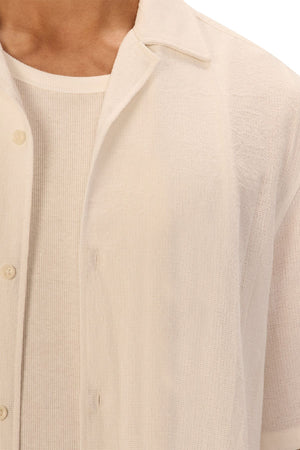 A close-up of a person wearing the Industrie The Marbella Short Sleeve Shirt, an off-white textured, relaxed-fit button-down over a matching ribbed T-shirt. Only the lower face, neck, and upper torso are visible, highlighting a casual everyday style.