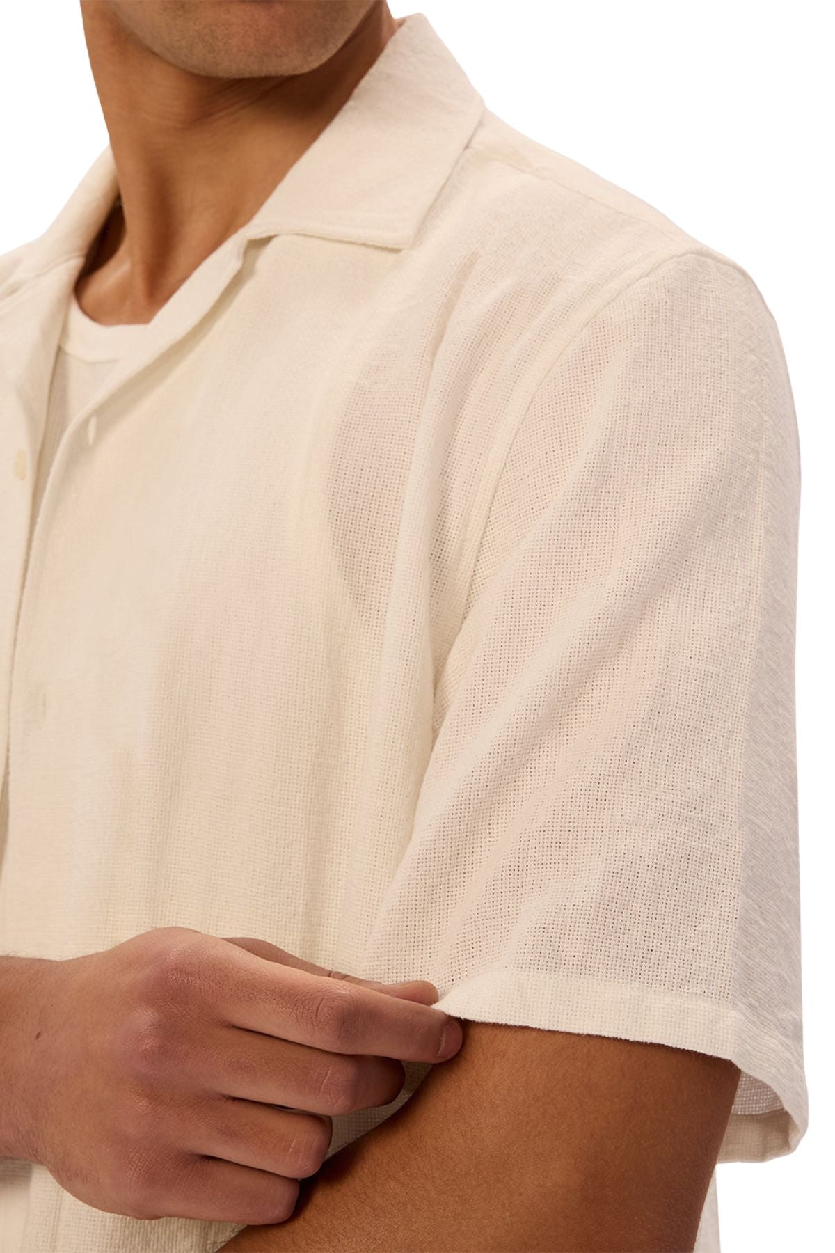 A person wears the Industrie The Marbella Short Sleeve Shirt in a relaxed fit, cream color, shown from shoulders to mid-torso, casually pulling at the sleeve; their face is partially out of frame to highlight an everyday style.