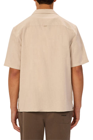 A person is seen from behind wearing the Industrie The Marbella Short Sleeve Shirt in light beige, made from lightweight textured fabric with a spread collar and short sleeves, paired with brown pants against a plain white background.