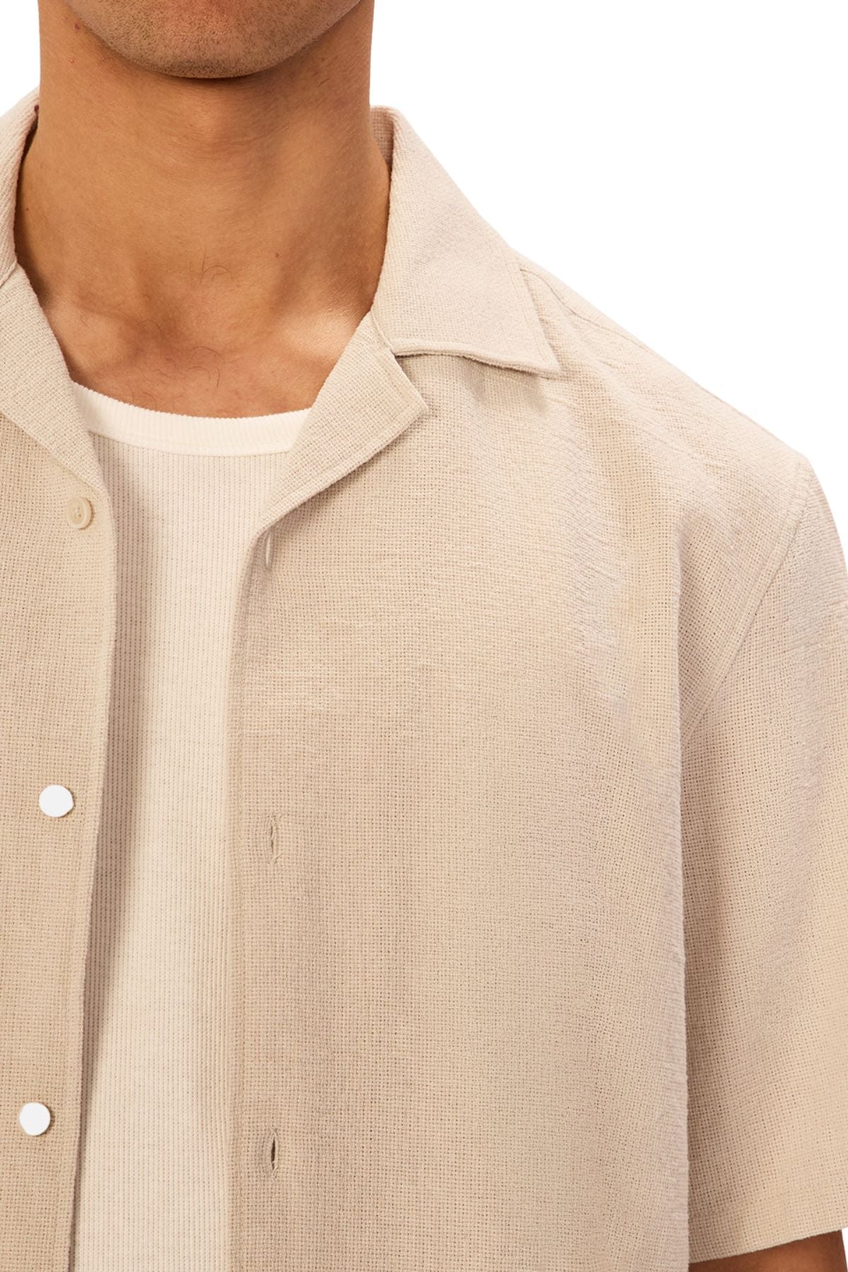 A person wears the Industrie The Marbella Short Sleeve Shirt in light beige, made from lightweight textured fabric, layered over a white ribbed t-shirt. Only the lower face, neck, and upper torso are visible.