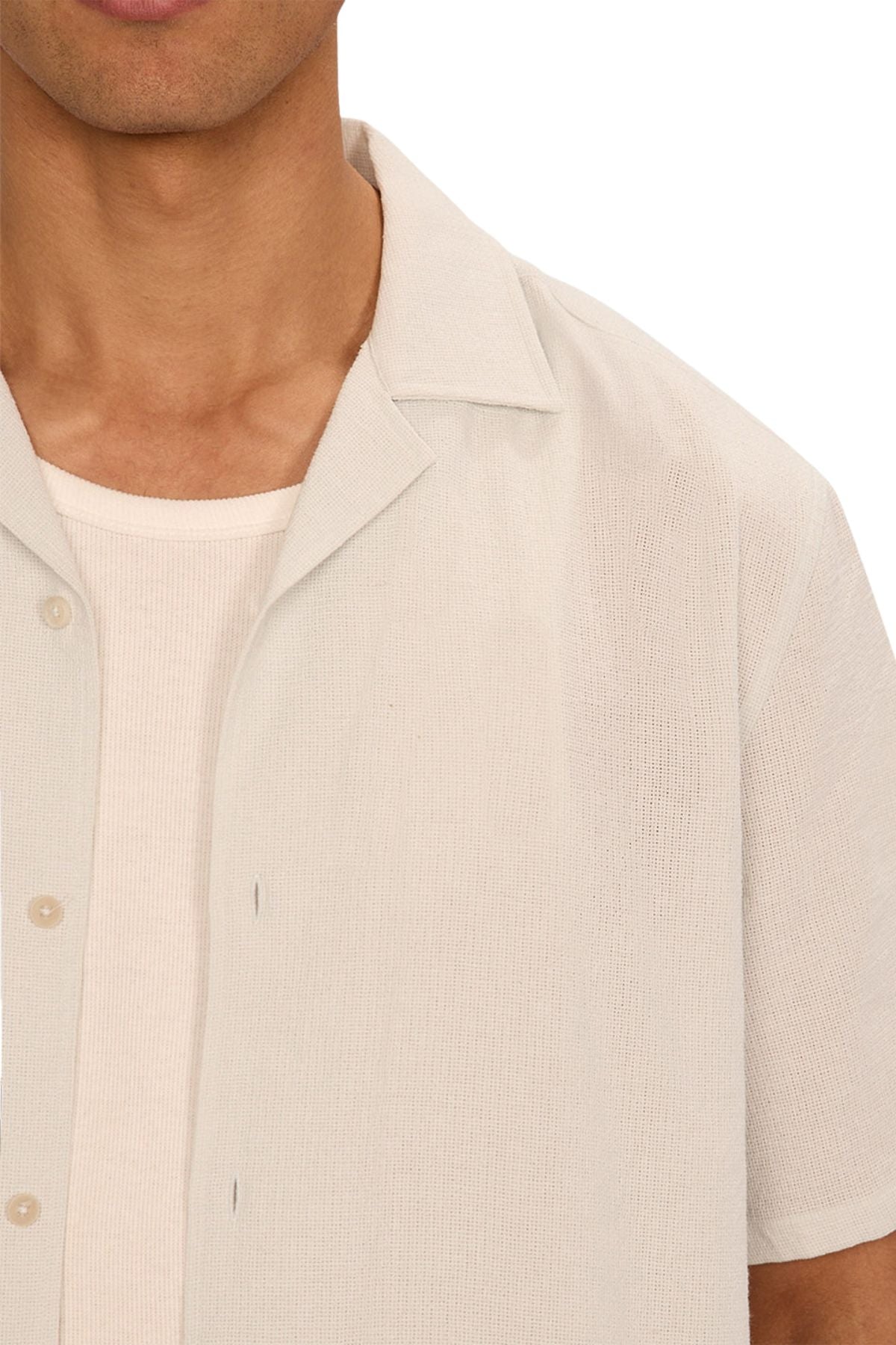 A close-up of a person wearing the Industrie The Marbella Short Sleeve Shirt, made from lightweight textured fabric, layered over a cream ribbed T-shirt. Only the lower face, neck, and upper torso are shown.
