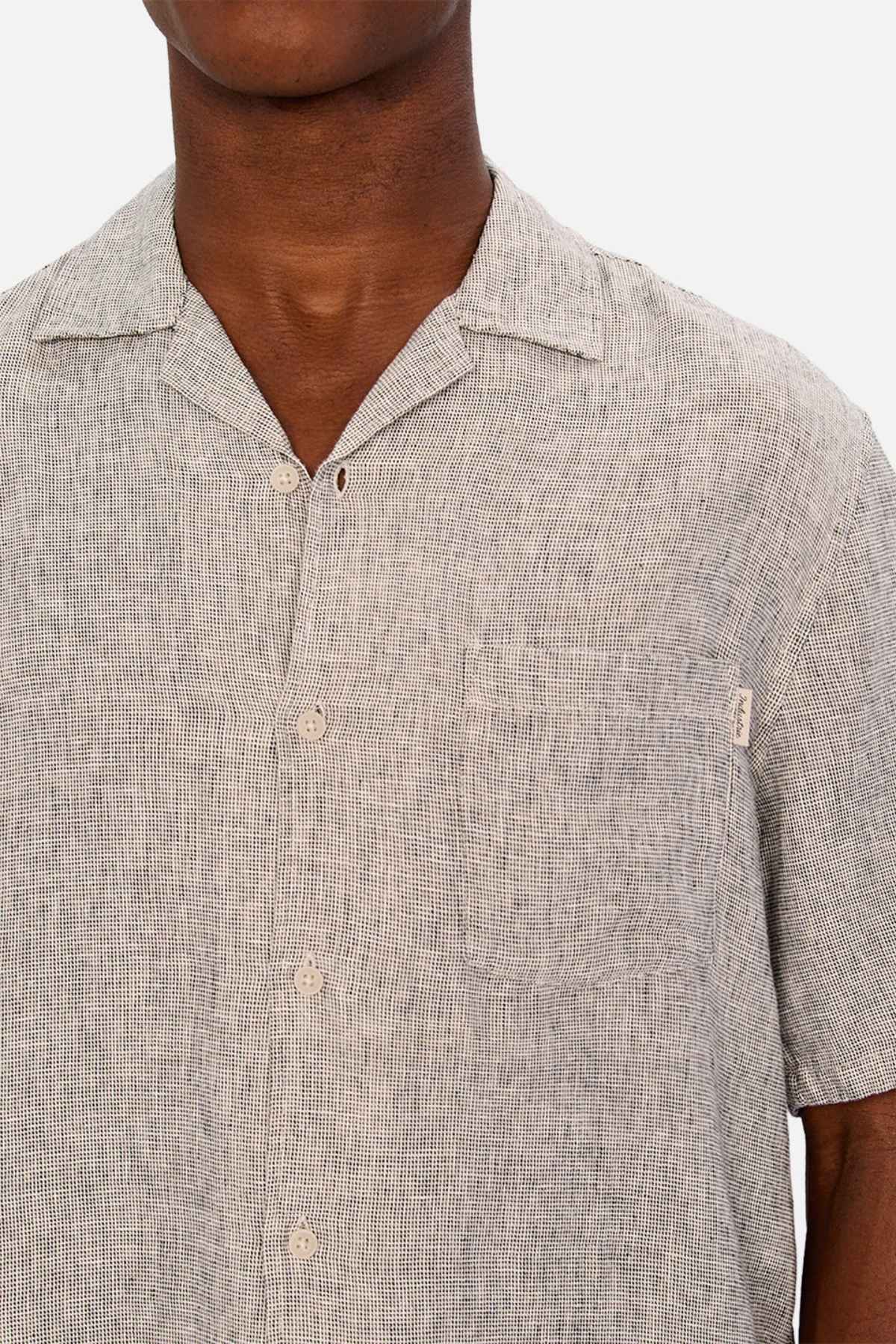 A person wearing the Industrie The Melrose Short Sleeve Shirt—a light gray, button-up linen Tencel shirt with a subtle texture, chest pocket, and relaxed collar. Only the upper torso and neck are shown.