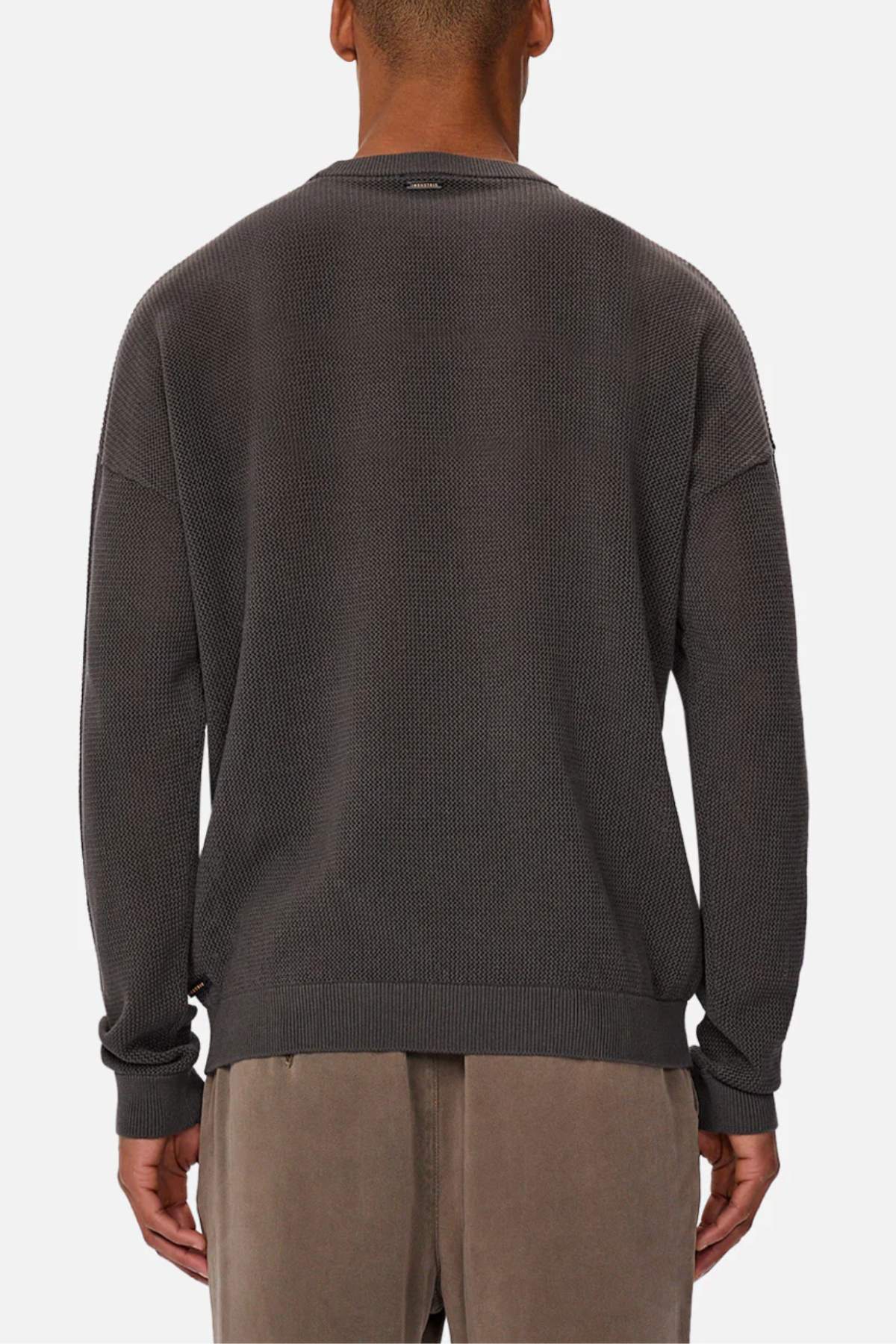 A person is shown from behind wearing the Industrie The Nanterre Crew Neck Knit, a textured dark gray oversized sweater, paired with light brown pants and standing against a plain white background.