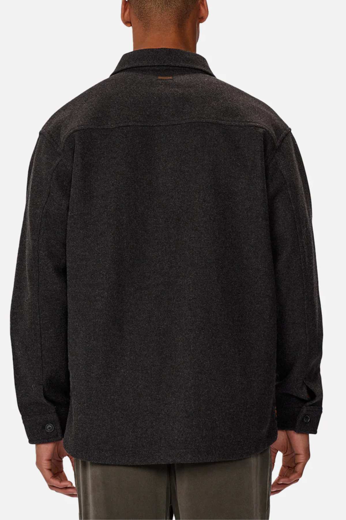 A person is shown from the back wearing the Industrie The New Coleman Jacket, which is a dark gray, relaxed-fit, long-sleeved shirt with a classic collar. They pair it with light gray pants against a plain white background.