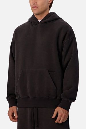 A person wears the Industrie The New Del Sur Fleece Hoodie in solid black, featuring an oversized fit with front pocket and hood. Only their torso and part of their face are visible against a plain light background, emphasizing the relaxed style.