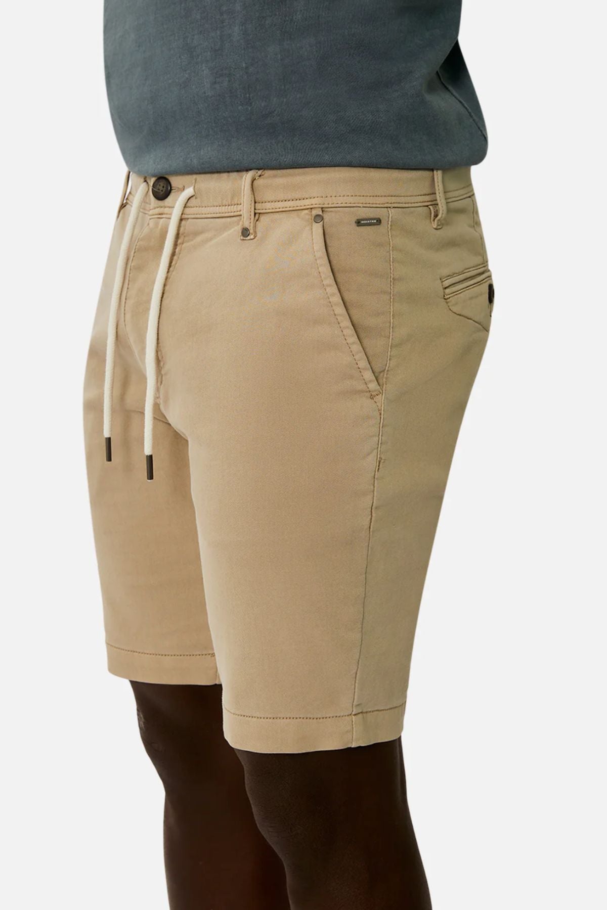 A person wearing Industrie The New Drifter Cuba Short in beige with a drawstring and side pockets, paired with a dark gray shirt against a plain white background.