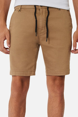 A person wears tan, knee-length Industrie The New Drifter Cuba Short with a black drawstring, side pockets, and belt loops, styled with a white tucked-in shirt. These fitted yet relaxed shorts are ideal for casual looks.