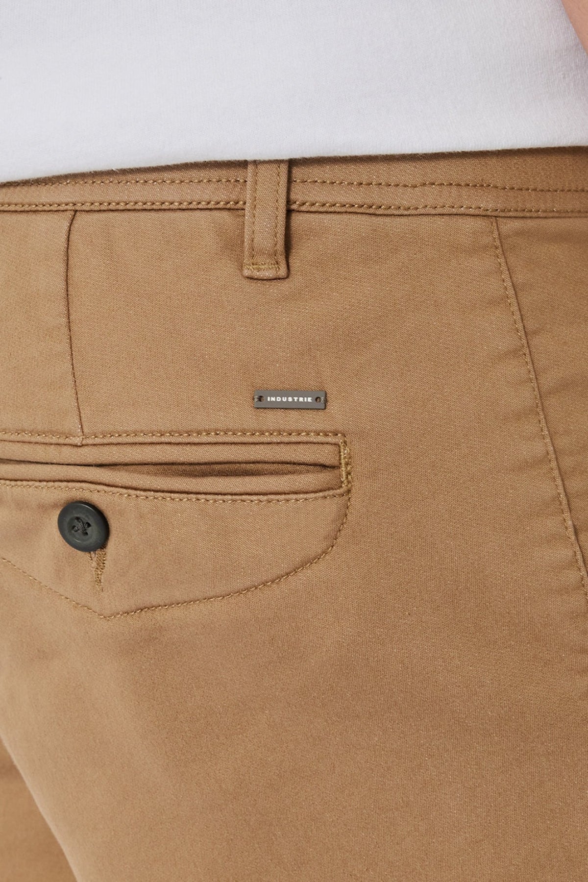 Close-up of the back of tan Industrie The New Drifter Cuba Short, featuring a black pocket button and metallic "INDUSTRY" label above, paired with a tucked-in white shirt for a casual, stylish look.