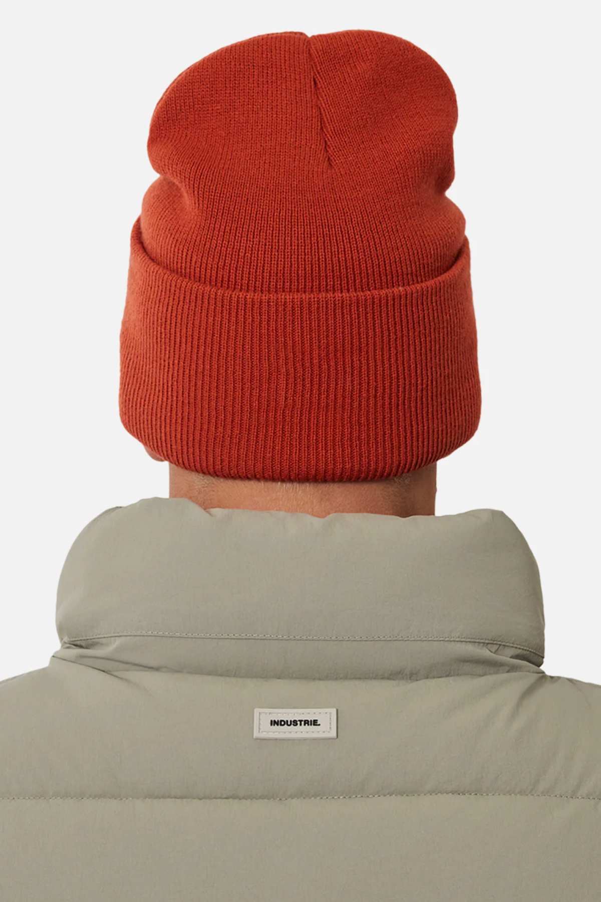 A person wearing a red knit beanie and a light gray Industrie The New Hanam Puffer Vest with quilted padding, photographed from behind against a plain background.