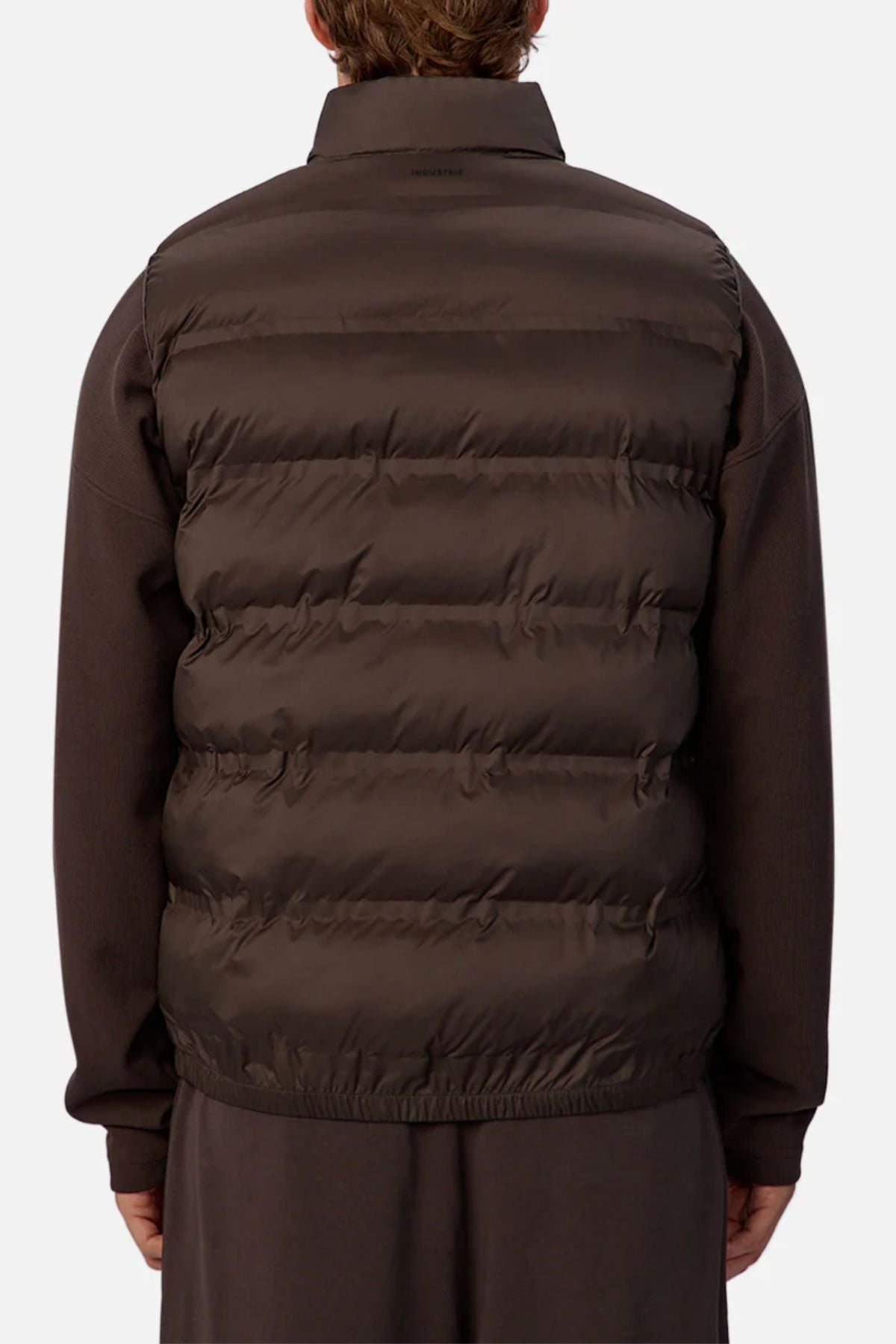 Someone wearing the Industrie The New Kyoto Puffer Vest, known for its featherlight design, over a long-sleeved brown shirt is shown from the back against a plain light background—ideal for cooler weather.