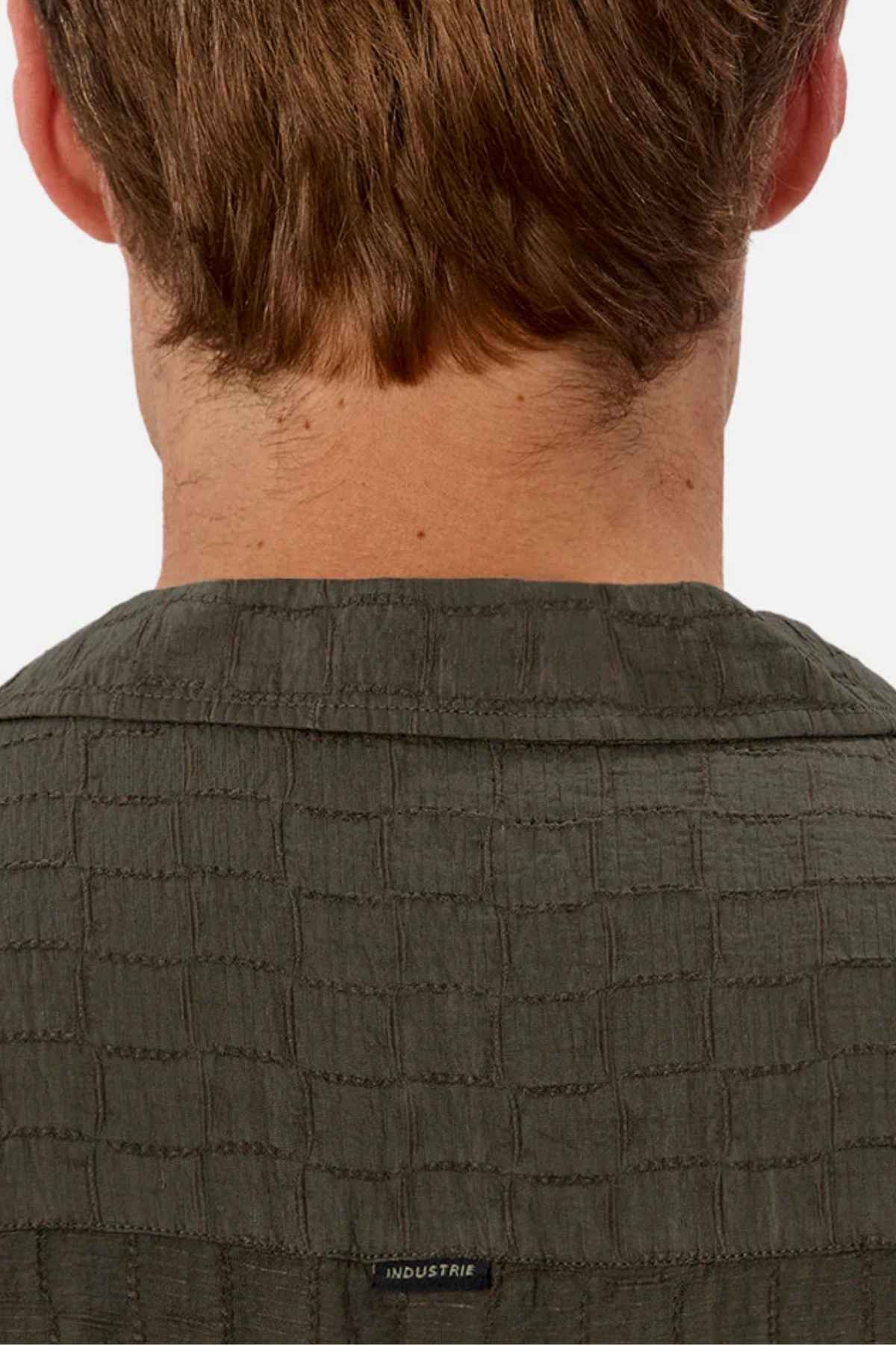 Seen from behind, a person with short brown hair is wearing the Industrie The New Ortigia Short Sleeve Shirt in a dark green jacquard pattern. The camp collar provides a hint of casual elegance, and the shirt features an "INDUSTRIE" label.