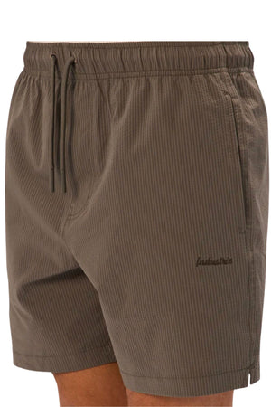 A close-up shows a person wearing Industrie The New Seersucker Swim Short in brown stripes, featuring an elastic waistband, drawstrings, subtle embroidered branding on the left leg, and made from quick-dry polyester.