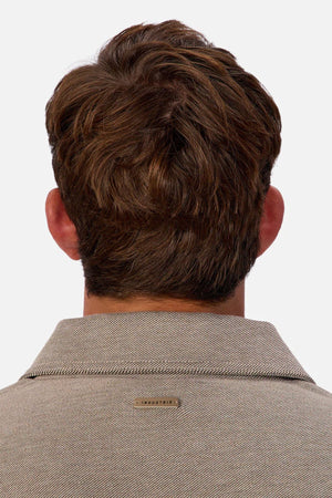 A man with short, wavy brown hair is seen from behind in a beige Industrie The New Westport Jacket featuring a small metallic “INDUSTRIE” tag on the back collar, set against a plain white background.