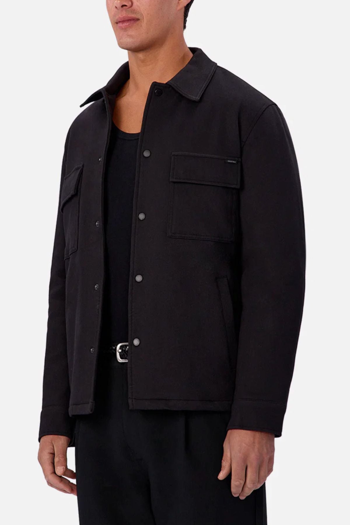 A man wearing the Industrie The New Westport Jacket, featuring flap pockets, over a black shirt and black pants stands against a plain light background.