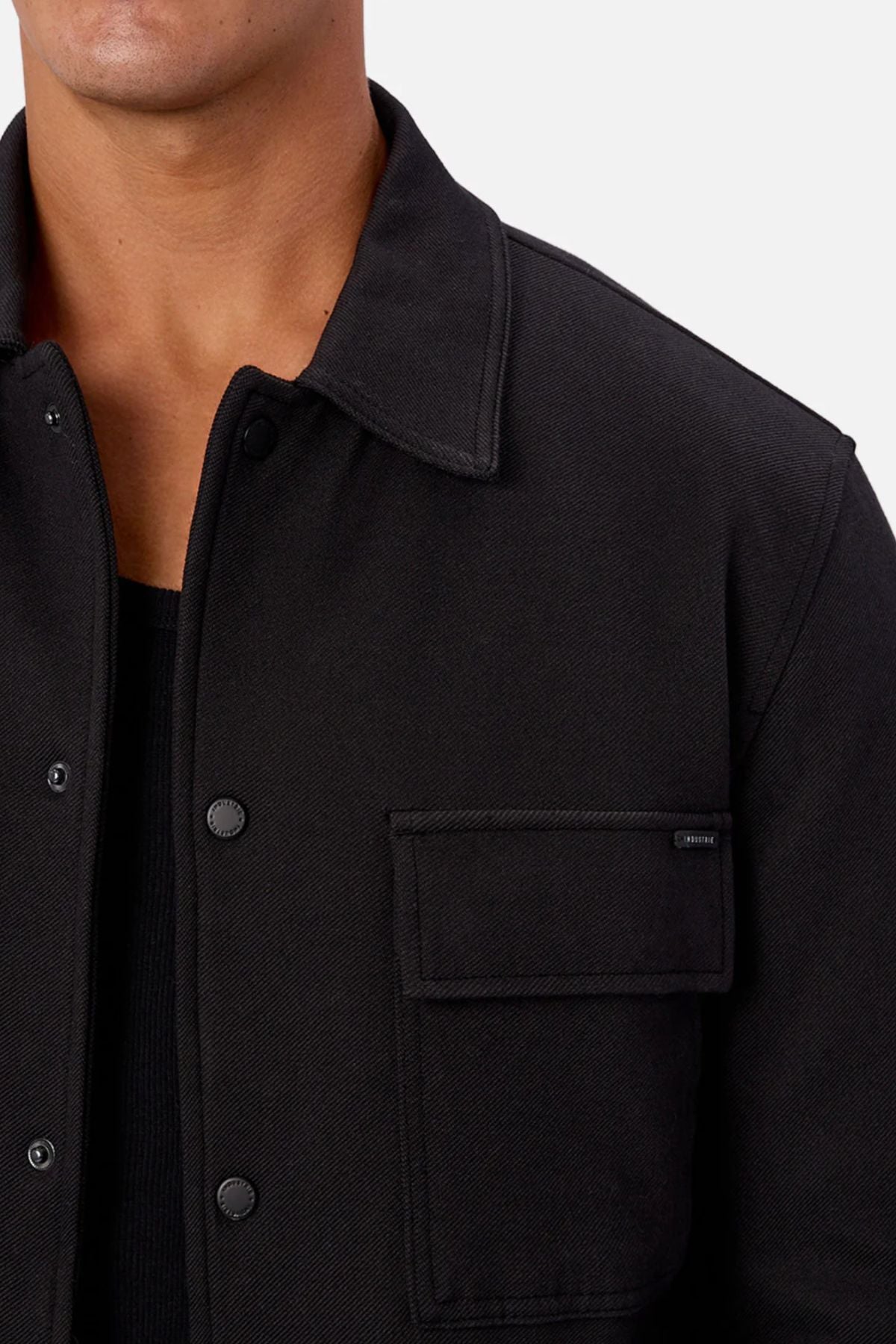 A person wearing the Industrie The New Westport Jacket, a smart-casual piece with snap buttons and a chest pocket over a black shirt; only their lower face and upper torso are shown.