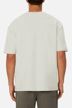 A person is shown from the back, wearing an oversized fit, light-colored Industrie The Newport Tee with short sleeves and dark shorts against a white background.