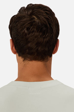 A man with short brown hair is seen from behind, wearing a light Industrie The Newport Tee with "INDUSTRIE" on the upper back. This heavyweight tee offers an oversized fit and is set against a plain, light background.