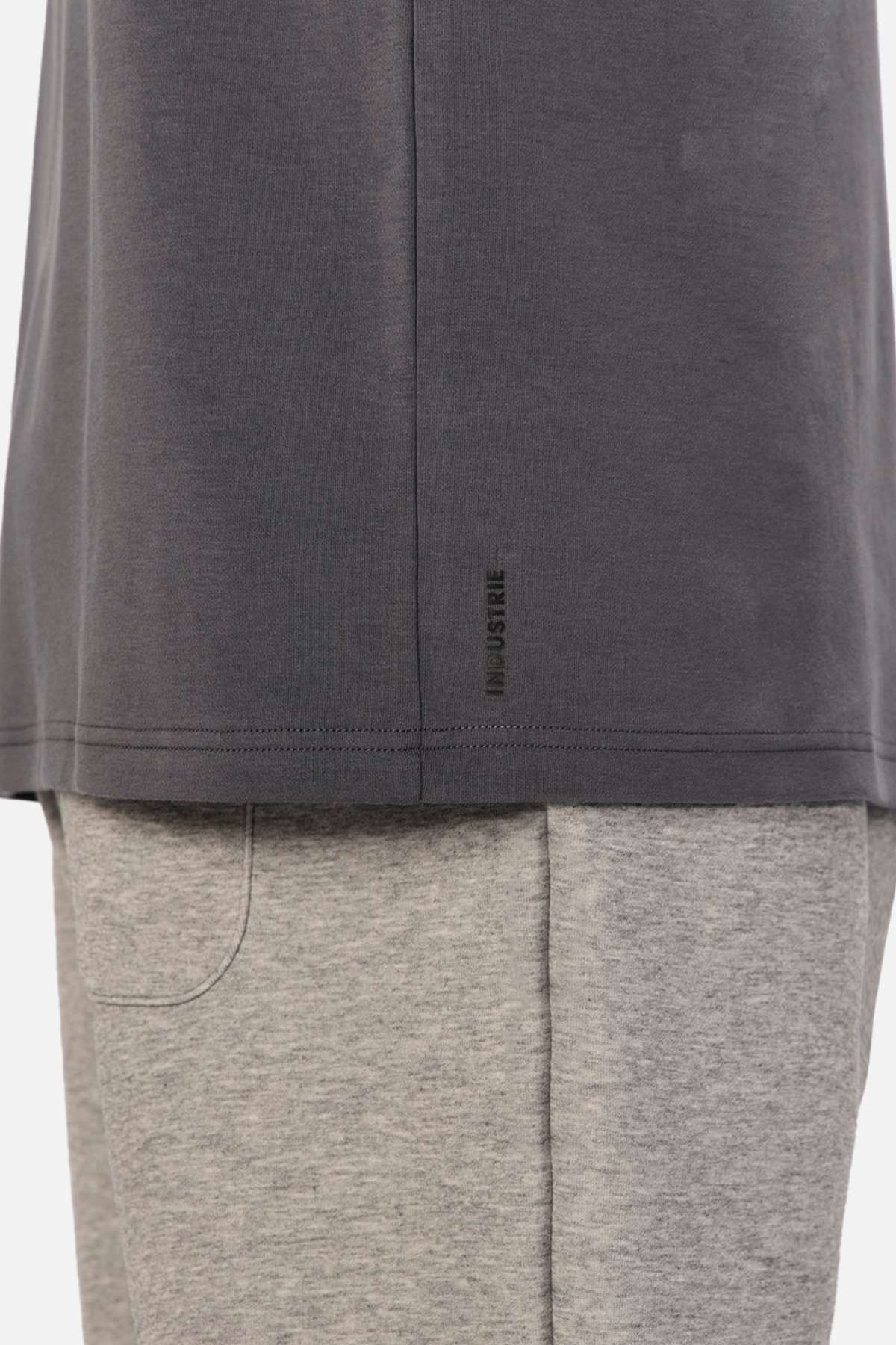 Close-up of a person wearing an oversized fit, dark grey Industrie The Newport Tee with a small logo near the hem, paired with light grey shorts. The image highlights the lower half of the 100% cotton shirt and the upper portion of the shorts.