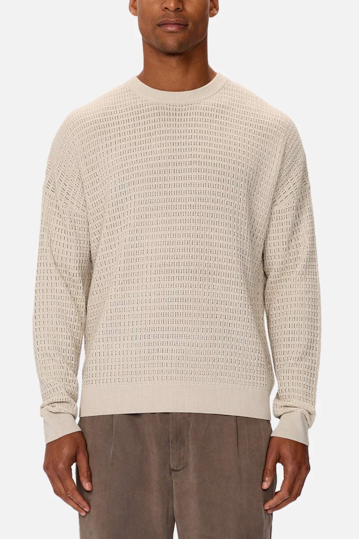 Someone is wearing the Industrie The Nunez Long Sleeve Knit, a textured beige sweater made from 100% cotton. It has long sleeves and a round neckline, paired with light brown trousers. The subtle pattern design contrasts beautifully against the plain white background.